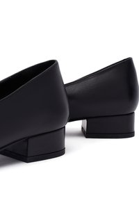 Scarpe nere in pelle con tacco basso e punta squadrata, dalla texture liscia. Presentano un modestissimo tacco a blocco e un design minimalista senza decorazioni.