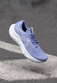 Hellblauer Laufschuh mit atmungsaktivem Mesh-Obermaterial, weißen Akzenten, gepolsteter Sohle und Schnürverschluss. Auffälliges Logo und strukturierte Oberfläche.