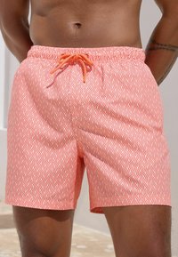 Pantaloni scurți de înot în nuanța corail, cu un model de valuri, având un elastic la talie și șnur de ajustare, confecționați dintr-un material ușor și texturat.