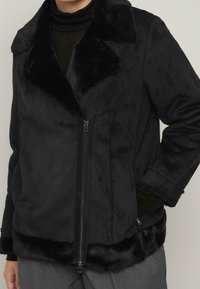 Giacca nera con colletto in pelliccia sintetica, chiusura con zip e tessuto morbido. Presenta tasche laterali e una vestibilità comoda.