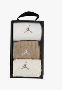 Trzy pary dzianinowych opasek na nadgarstek w odcieniach beżowym, kremowym i białym, z wyszywanymi logo Jumpman. Zapakowane w przezroczyste pudełko z czarną rączką.