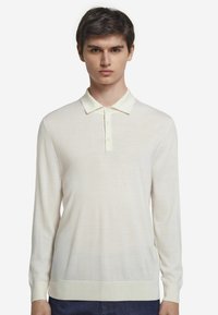 Ljuskrämfärgad långärmad pikétröja med treknapplås, ribbade ärmslut och ett mjukt, texturerat tyg.