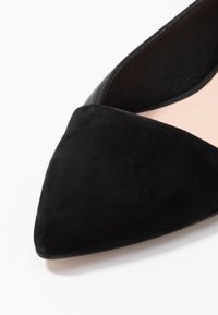 Chaussure noire en daim à bout pointu avec une tige en cuir lisse et une texture douce contrastante. Présente un design épuré et minimaliste avec une semelle étroite.