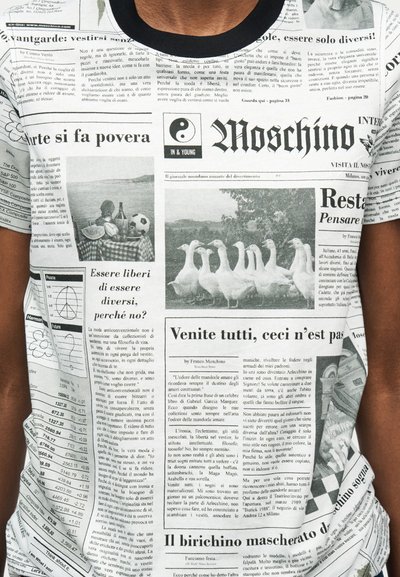 Άνδρας που φοράει μπλουζάκι με τύπωμα εφημερίδας, το οποίο περιλαμβάνει κείμενο, φωτογραφία με χήνες, πικνίκ με ποδόσφαιρο και σύμβολο γιν-γιανγκ κοντά στον γιακά.