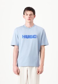 Light blue cotton t-shirt with short sleeves and a crew neck, featuring a bold, overlapping "HUGO" logo in darker blue across the chest.