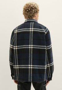 Jachetă din flanel în carouri bleumarin, realizată dintr-un material moale, cu pătrățele albe și negre, guler standard și buzunare laterale.
