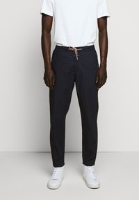 Pantalon léger bleu marine avec une ceinture élastique et un cordon de serrage. Accompagné de baskets blanches et d'un t-shirt blanc basique.