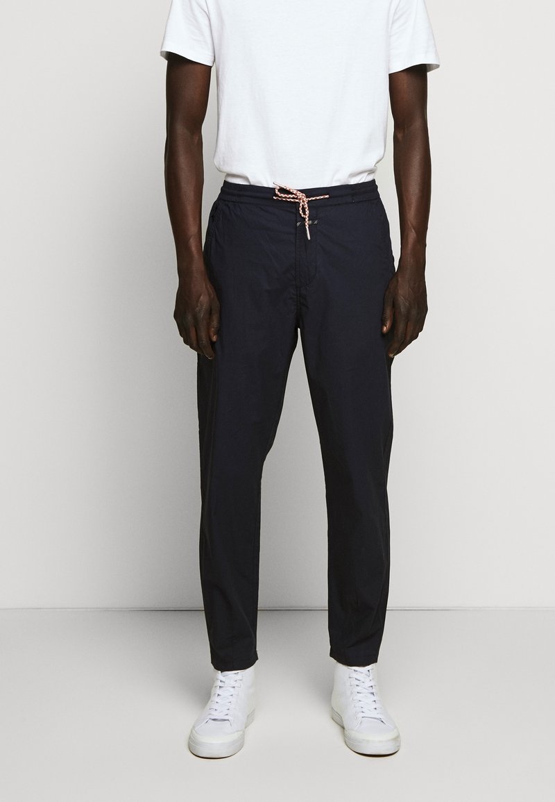 Pantalon léger bleu marine avec une ceinture élastique et un cordon de serrage. Accompagné de baskets blanches et d'un t-shirt blanc basique.