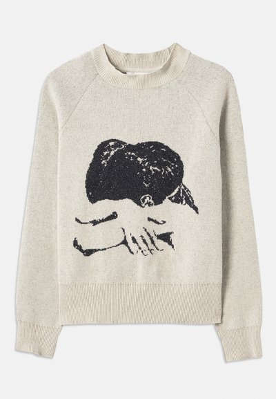 Beige pulóver, texturált felülettel, fekete grafikával, amely egy asztalon pihenő kezeket ábrázol. Kerek nyakkivágás és bordás mandzsetták jellemzik.