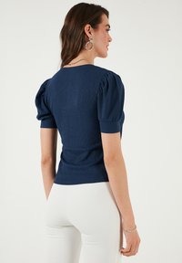 Marineblaues geripptes Shirt mit kurzen Puffärmeln, taillierter Passform und rundem Ausschnitt. Trägt man mit weißen Hosen. Keine sichtbaren Muster oder Akzente.