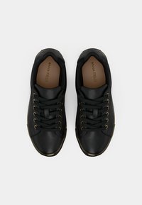 Sneaker in pelle nera con punta arrotondata, dotate di occhielli e lacci in tonalità dorata e una texture liscia. L'interno ha una soletta marchiata di colore beige.