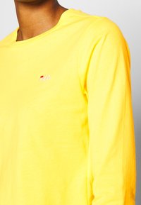 Långärmad gul T-shirt i mjukt bomull. Har en liten, broderad Fila-logotyp i röd och vit på bröstet. Rundhalsad design.