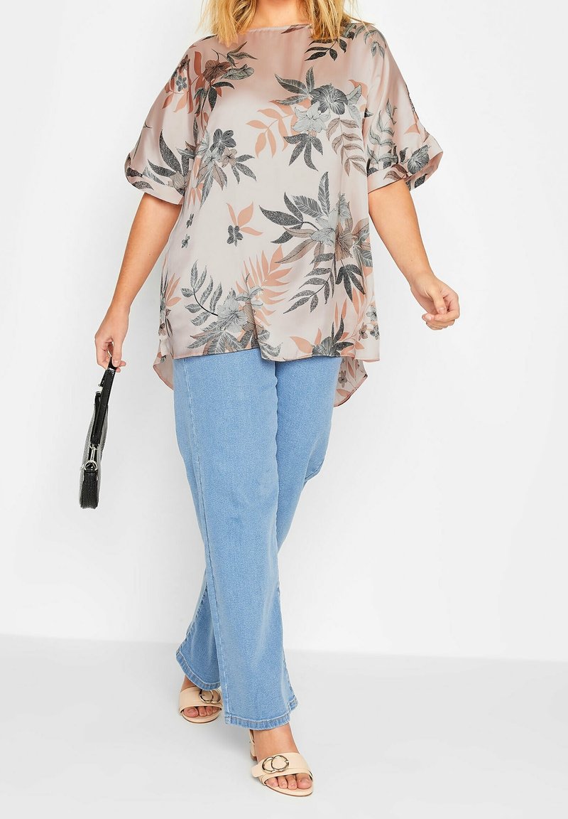 Hihaton pusero vaaleanpunaisella ja harmaalla pastellisella kukkakuviolla, yhdistettynä vaaleansinisiin farkkuihin ja beigeihin liukuviin sandaaleihin. Musta käsilaukku pidetään kädessä.