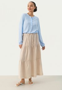 Lyseblå langærmet skjorte med knaplukning, parret med en beige lagdelt maxiskirt. Outfittet har en afslappet pasform og er suppleret med flip-flops.
