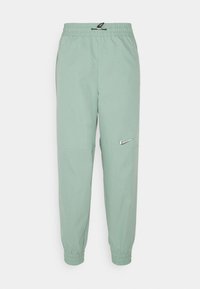 Ljust gröna Nike-joggingbyxor med elastiskt midjeband och muddar, justerbar dragsko och silverfärgad Nike-logga på höger lår.