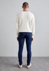 Biały prążkowany sweter z długimi rękawami, zestawiony z dopasowanymi ciemnoniebieskimi jeansami i jasnymi trampkami, widok od tyłu.