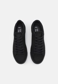 Svarta sneakers tillverkade av slätt material med platta skosnören. Har en minimal design och rund tå. Etiketten säger "Garment Project."