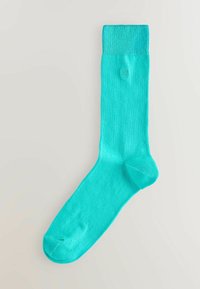 Turkizna nogavica z rebrastim robom, gladko teksturo in ojačano konico. Enostaven dizajn, primeren za vsakodnevno nošenje. Podrobnost z logotipom blizu roba.