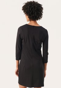 Robe noire à manches trois-quarts, avec un dos en forme d'encolure arrondie, une coupe ajustée et une fermeture éclair dans le dos. Tissu lisse, extensible avec une texture unie.