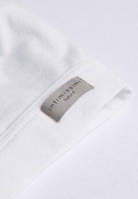 Vitt bomullstyg med en slät textur, med en grå etikett som har texten "intimissimi" och "Natural" i elegant typsnitt.