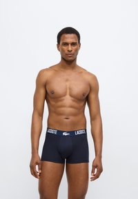 Boxers bleu marine avec un logo Lacoste blanc contrastant sur la ceinture élastique, fabriqués dans un tissu lisse et doux, coupe ajustée.