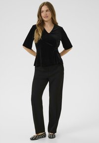 Top in velluto nero con scollo a V e maniche corte, abbinato a pantaloni neri e ballerine nere con un design borchiato.