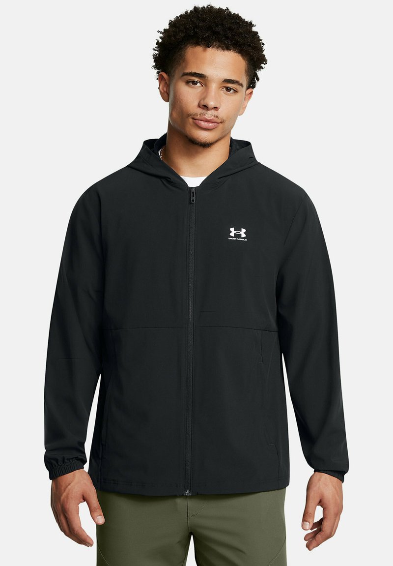 Melna zip-up jaka, kas izgatavota no viegla materiāla, aprīkota ar kapuci, elastīgām piedurknēm un mazu baltu logotipu uz kreisā krūts.