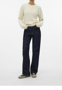 Helle Creme, strukturierter Pullover mit Rundhalsausschnitt; dunkelblaue, hochtaillierte weite Jeans; graue und schwarze Sneakers mit Schnürsenkeln.