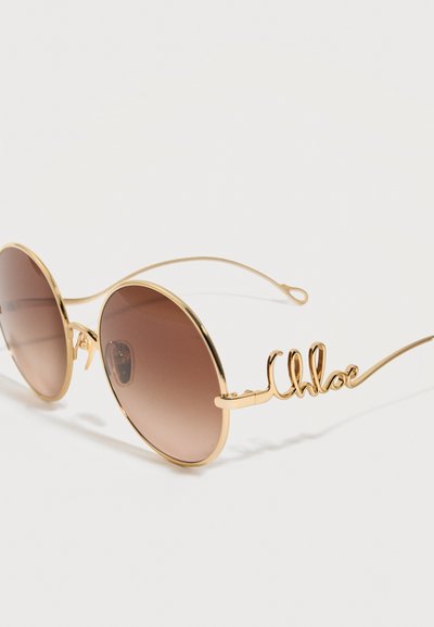 Στρογγυλά γυαλιά ηλίου με καφέ φακούς διαβάθμισης και λεπτά μεταλλικά χρυσά πλαίσια, με διακοσμητική χρυσή σύρμα που σχηματίζει τη λέξη «Chloé» στο μπράτσο.