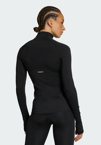 Crna dugorukava atletska majica s visokim ovratnikom, glatke teksture i prilagođenog dizajna. Sadrži "TECHFIT" logotip na leđima.