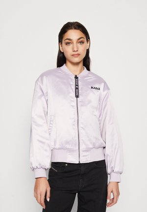 Lichtpaarse satijnen bomberjack met een rits aan de voorkant, geribde boorden en een logo op de linkerborst; gestyled met zwarte jeans.