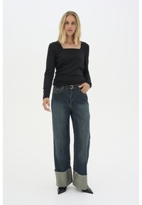 Black long-sleeve top with a square neckline paired with wide-leg denim jeans featuring frayed, contrasting green cuffs. Black pointed heels.