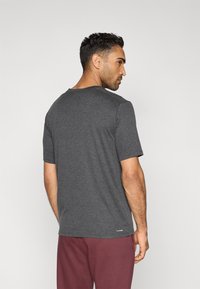 Γκρι κοντομάνικο T-shirt με στρογγυλή λαιμόκοψη και υφασμάτινη υφή. Φοράται με μπορντό παντελόνι. Διακριτική λεπτομέρεια λογότυπου στο τελείωμα.