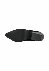 Zapato de tacón negro con puntera afilada y parte superior de tela texturizada. La suela de goma presenta ranuras horizontales para ofrecer tracción y soporte.