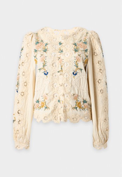 Blouse en dentelle crème avec de longues manches bouffantes et une broderie florale multicolore complexe sur le devant et les manches.