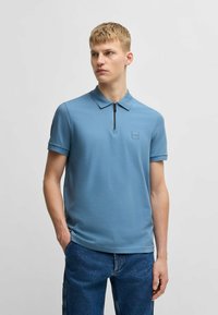 Ljusblå polo skjorta med dragkedja i kragen, korta ärmar och strukturerad tyg med en liten logopatch på bröstet.