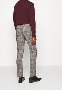 Karierter Hosen in Beige, Braun und Marineblau, mit schmaler Passform, flachem Bund und Eingrifftaschen, kombiniert mit schwarzen Schuhen.