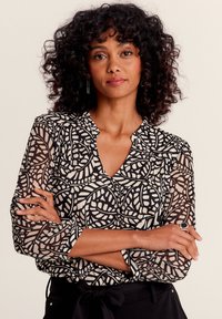 Schwarze und cremefarbene Bluse mit einem Blattmuster, langen transparenten Ärmeln, V-Ausschnitt, strukturiertem Stoff und geknöpften Handgelenken.