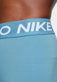 Leggings deportivos azules con una ancha cinturilla elástica en la que se lee "NIKE" en letras blancas. La tela es suave y elástica.