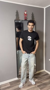 Must t-särk ringikujulise graafilise disainiga, helerohelised teksad ja hallid tossud, seisab tavalise taustaga peegli ees.