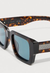 Kvadratna sončna očala temno želvje barve okvirjev, modrimi stekli in teksturiranim srebrnim poudarkom na straneh. Model: Calvin Klein 150.