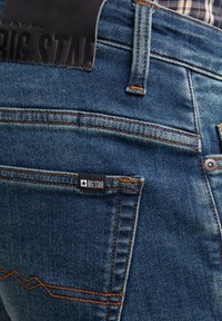 Jeans in denim blu con una texture distintiva, cuciture arancioni, una patch in pelle con la scritta "BIG STAR" e un piccolo etichetta del marchio sulla tasca posteriore.