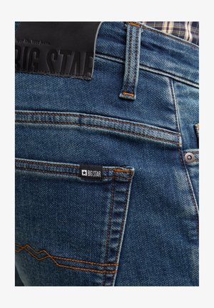 Jeans in denim blu con una texture distintiva, cuciture arancioni, una patch in pelle con la scritta "BIG STAR" e un piccolo etichetta del marchio sulla tasca posteriore.