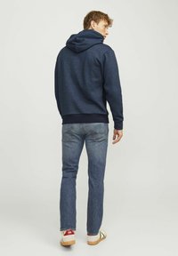 Sudadera con capucha azul marino de acabado texturizado, combinada con jeans de pierna recta. Costuras visibles en los bolsillos traseros y zapatos casuales.