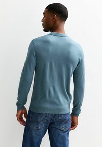 Aansluitende, langmouwen trui van zacht teal stof, met een ronde halslijn en geribbelde manchetten. Gecombineerd met blauwe denim jeans met achterzakken.