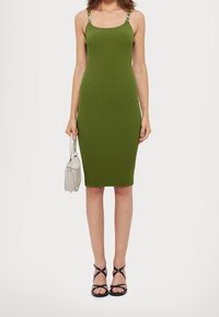 Robe midi côtelée vert olive avec fines bretelles et accessoires argentés. Associée à un sac léger et des escarpins noirs à brides.