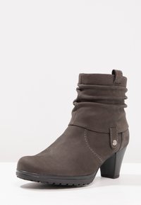 Bottine en cuir gris avec un design ample, bout arrondi, talon empilé et un détail décoratif de bouton-pression sur le côté.