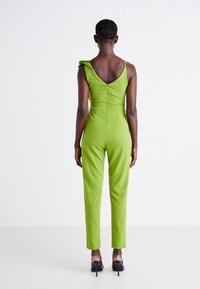 Žalia, be rankovių šokinė, su prigludusia siluetu, volangų detalėmis ant pečių ir žemu nugaros kirpimu. Lygus audinys ir užtrauktukas nugarinėje pusėje.