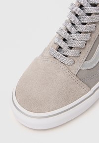 Light gray suede sneaker featuring textured upper, silver lace closures, and a white rubber sole with gray accents along the edge.