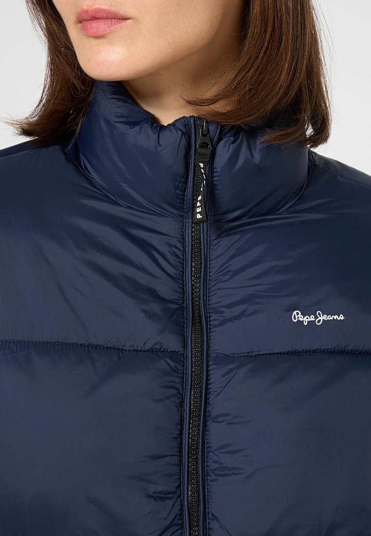 Chaqueta de plumas azul marino con cuello alto, cierre de cremallera y detalle del logotipo en blanco en el pecho. Tejido suave y brillante con un patrón acolchado.